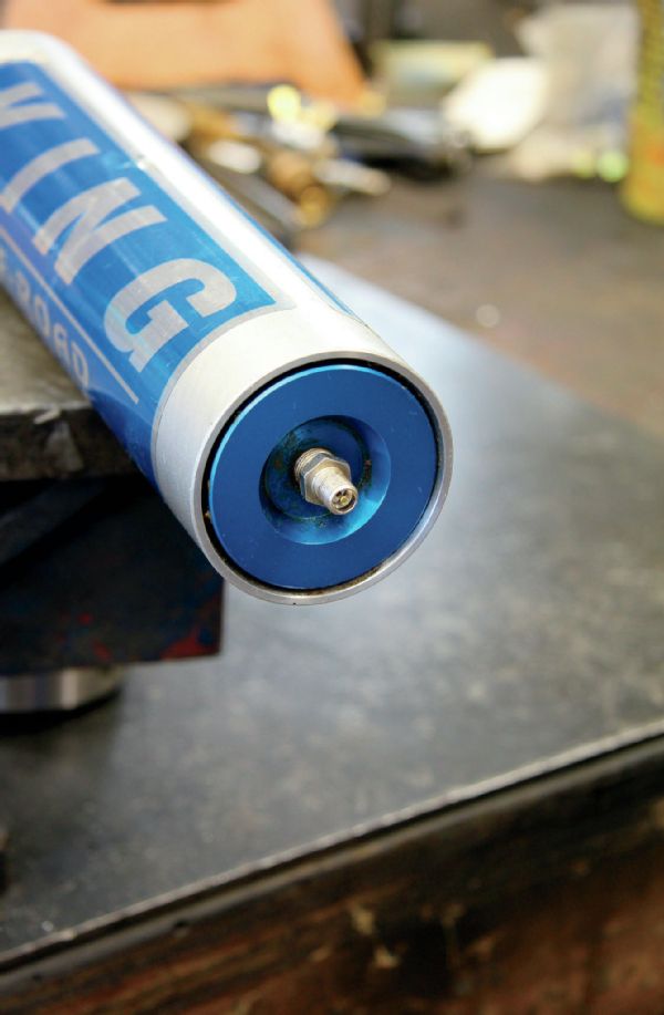 Once you have the coilover removed from the rig, secure it in your bench vise and mount it vertically with the body side down. After you lock the shock in place, purge the nitrogen from the shock by pressing down on the Schrader valve on the end of reservoir.
